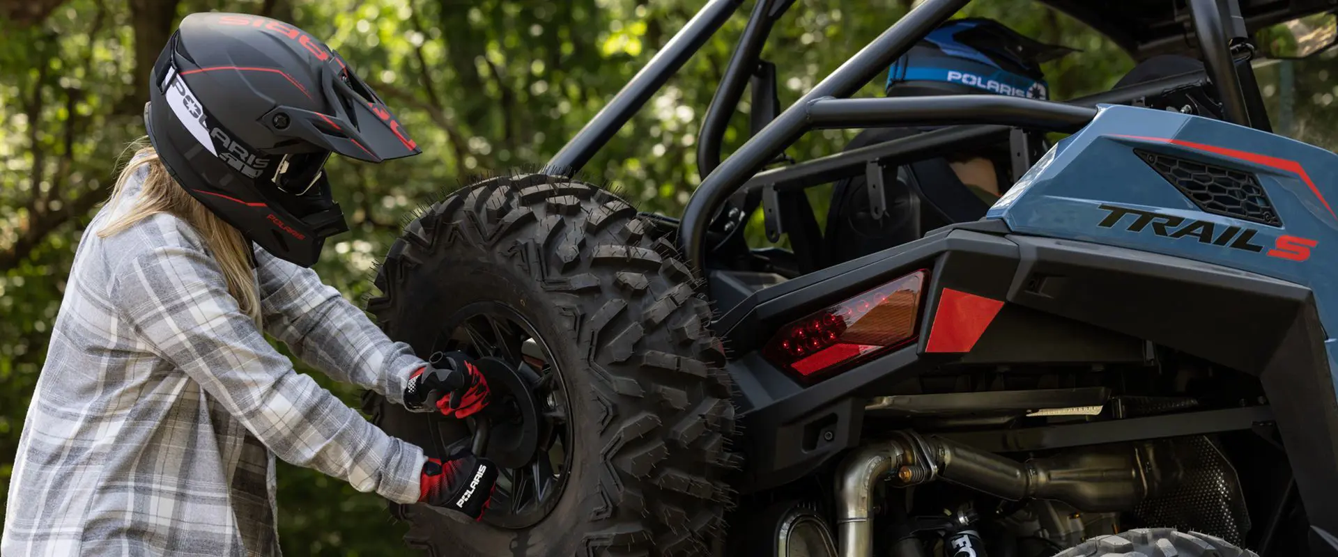 person putting a tire on the rear end of a polaris rzr trail s side by side