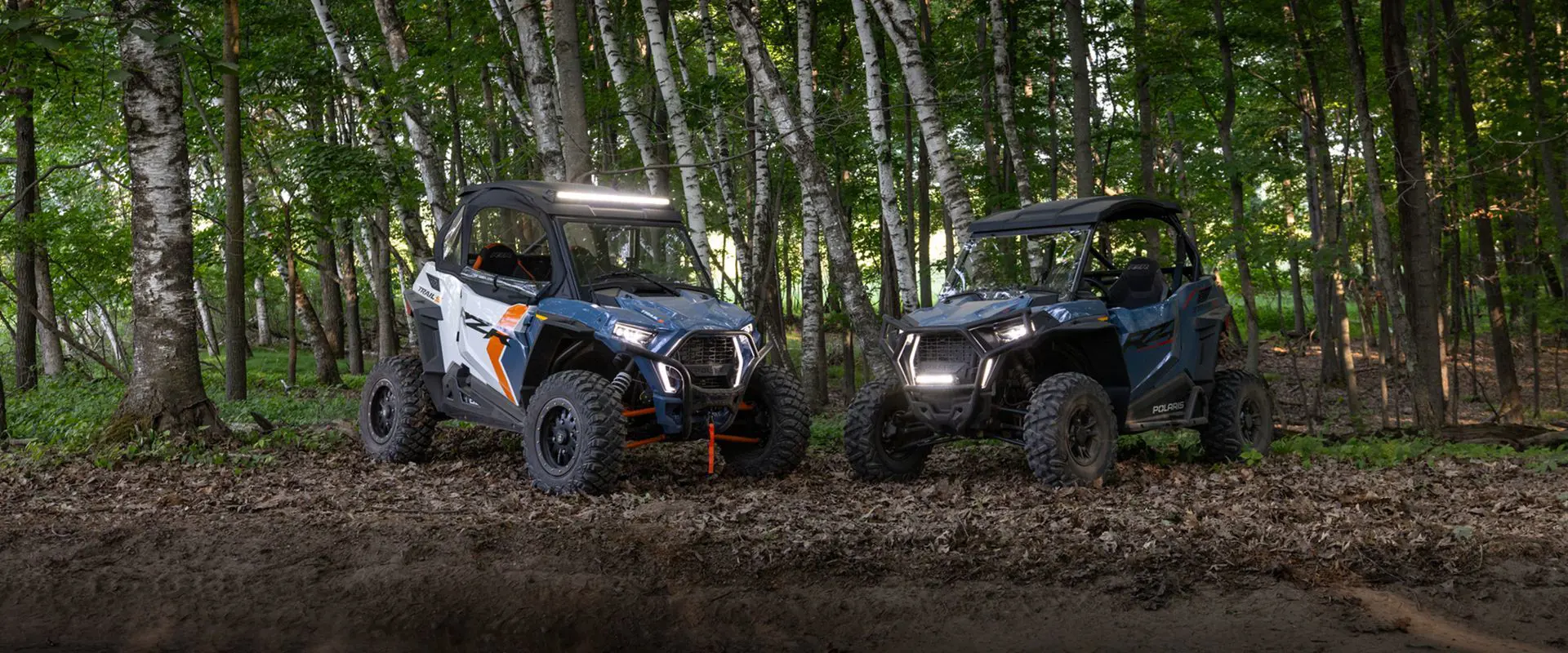 2 polaris rzr trail s side by sides parked near a treeline