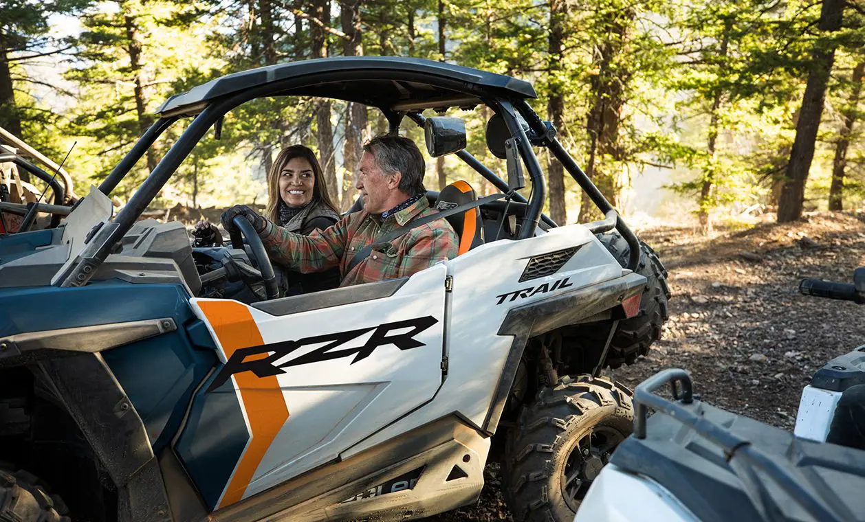2 people riding in a polaris rzr trail side by side