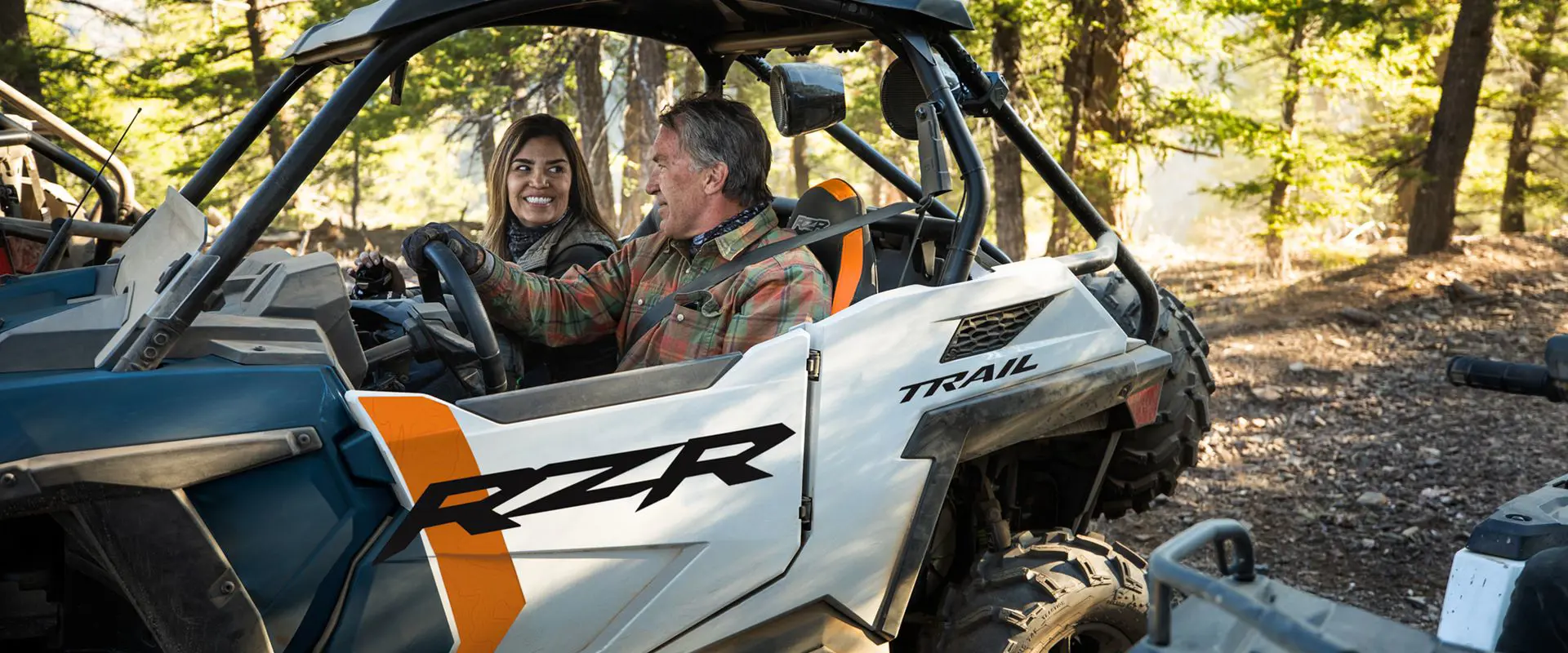 2 people riding in a polaris rzr trail side by side