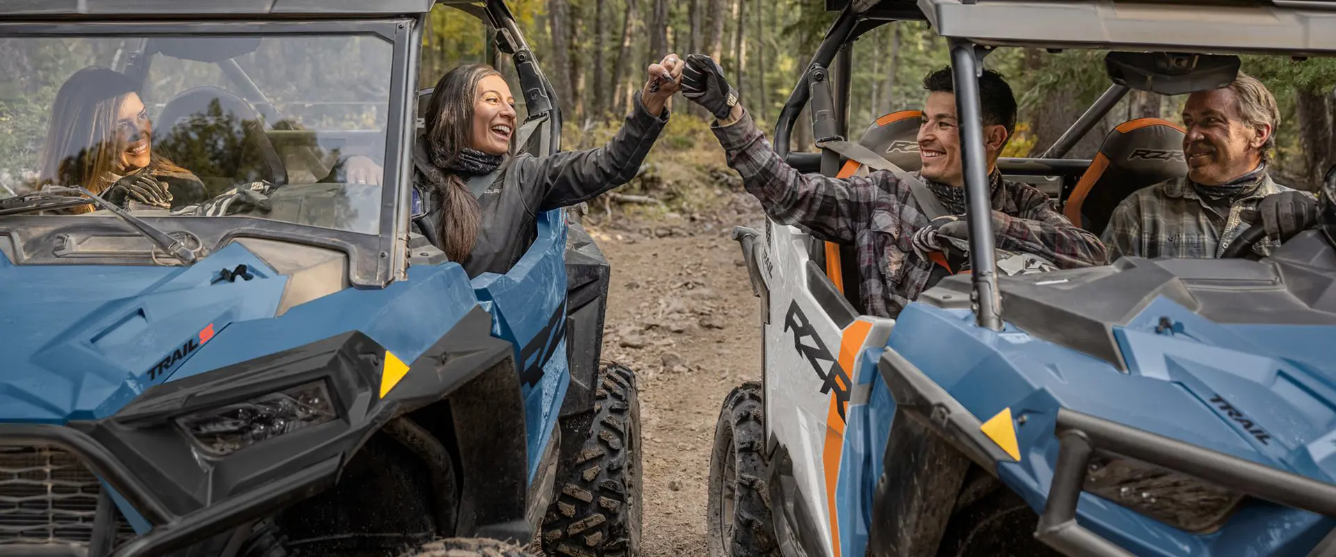 people smiling and pounding fists in their polaris rzr trail side by sides