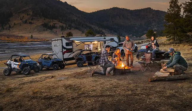 people hanging around a campfire with their rzr trail side by sides in the background