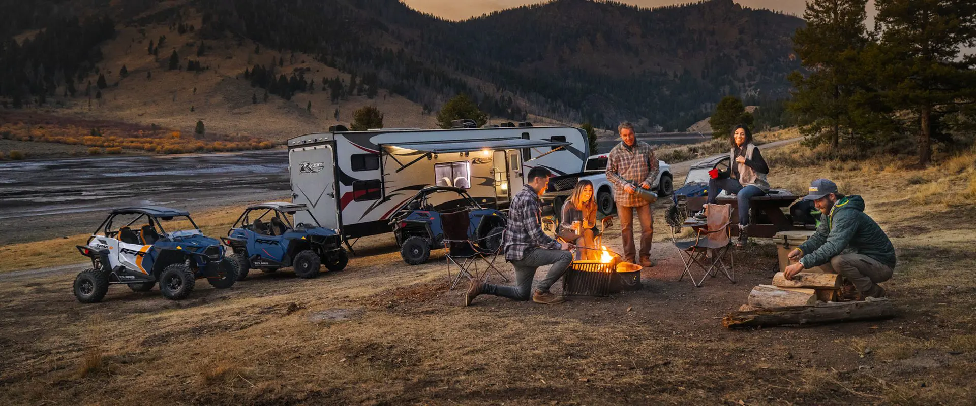 people hanging around a campfire with their rzr trail side by sides in the background