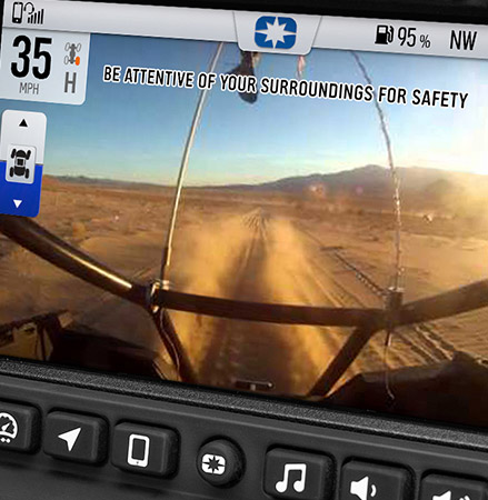 A Polaris RIDE COMMAND screen displays a live camera feed from a RZR vehicle driving on a dusty desert trail, with a safety warning BE ATTENTIVE OF YOUR SURROUNDINGS FOR SAFETY overlaid on the screen.