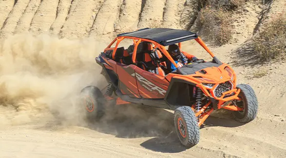 Side view of a 2025 Polaris RZR Pro R Factory Armored Edition side-by-side driving through the desert.