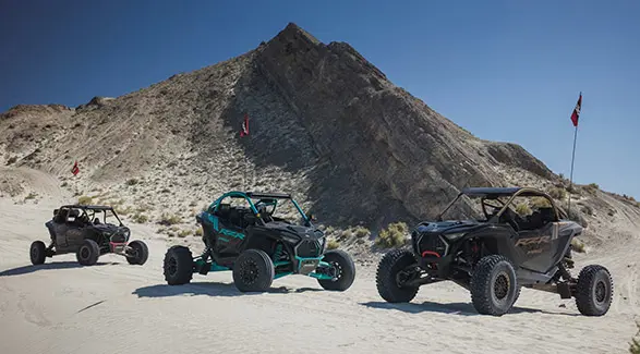 Three 2025 Polaris RZR Pro R side-by-sides parked near a mountain in the desert.