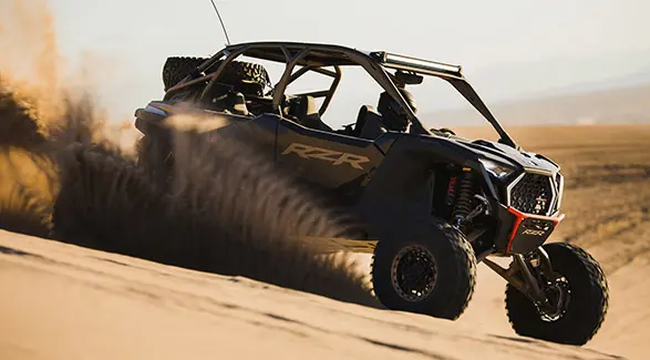 Side profile of a 2025 Polaris RZR Pro R 4 side-by-side throwing sand in the desert.
