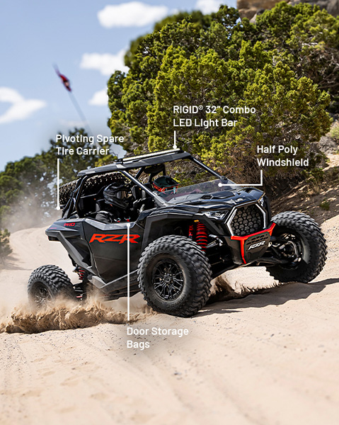 Pivoting spare tire carrier, RIGID 32-inch combo LED light bar, half poly windshield and door storage bag accessories from the Desert Package installed on a 2025 Polaris RZR Pro S side-by-side.