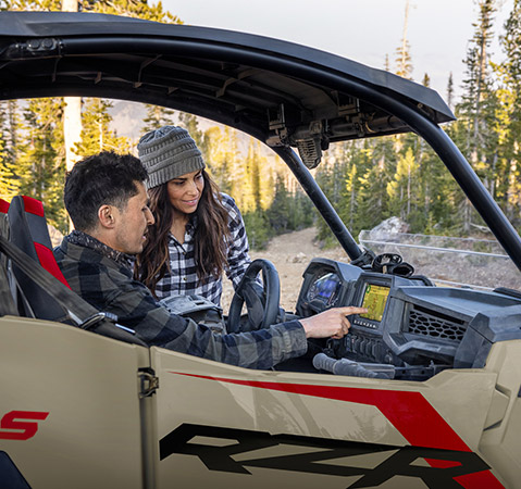 Man showing a woman features on the 7-inch RIDE COMMAND touch display in a 2025 Polaris RZR Trail side-by-side.