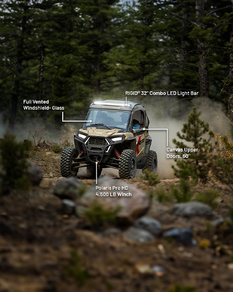 Full vented glass windshield, RIGID 32-inch combo LED light bar, 60-inch canvas upper doors, and Polaris Pro HD 4,500 lb. winch accessories from the Adventurer Package installed on a 2025 Polaris RZR Trail side-by-side.