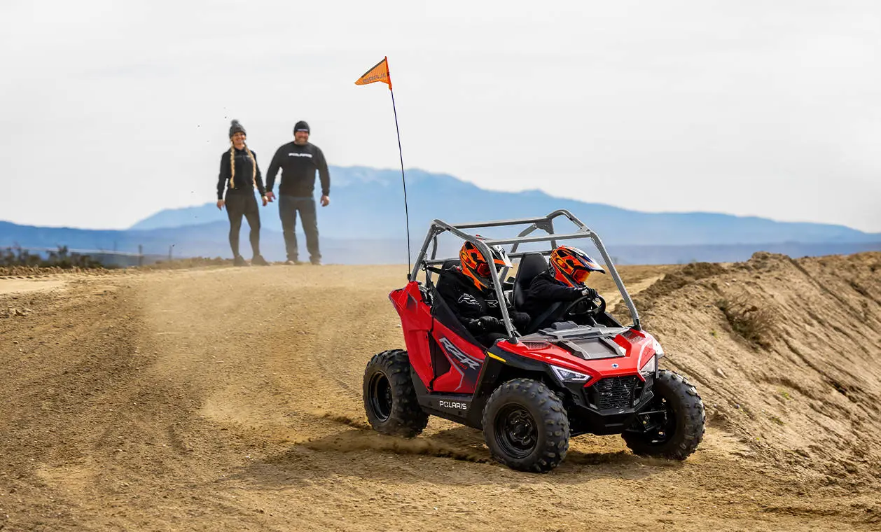 2 parents watching their kids drive a 2026 Polaris RZR 200 EFI youth SxS.