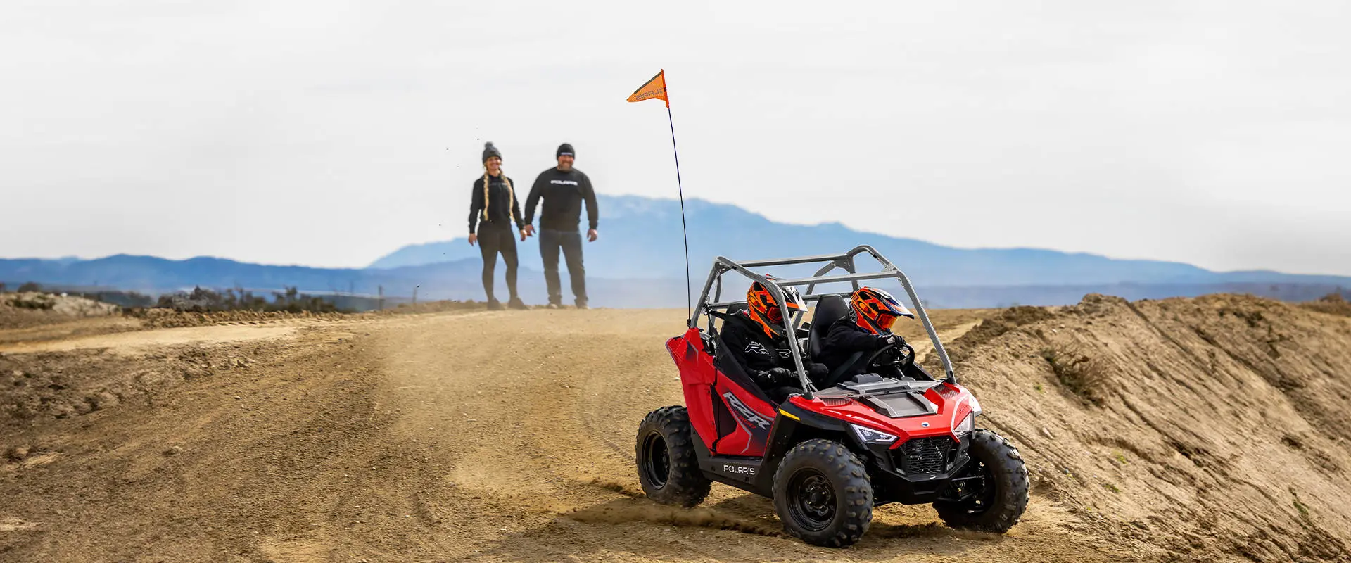 2 parents watching their kids drive a 2026 Polaris RZR 200 EFI youth SxS.