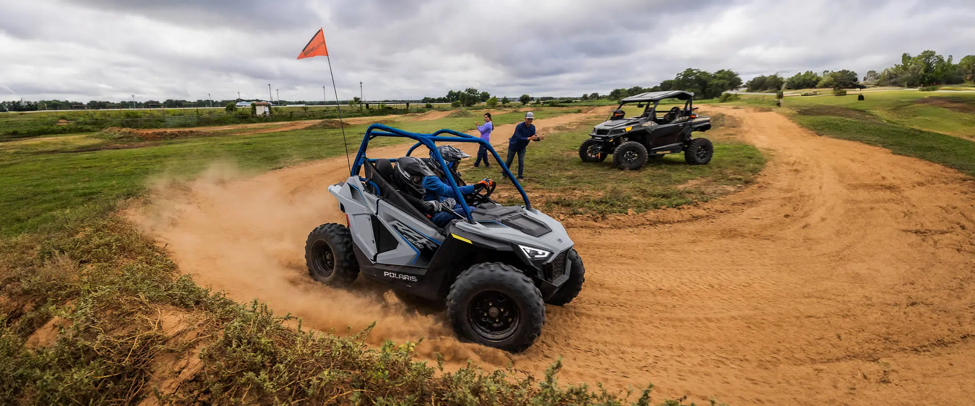 Side view of 2 kids in a 2026 Polaris RZR 200 EFI youth SxS driving on an open course.