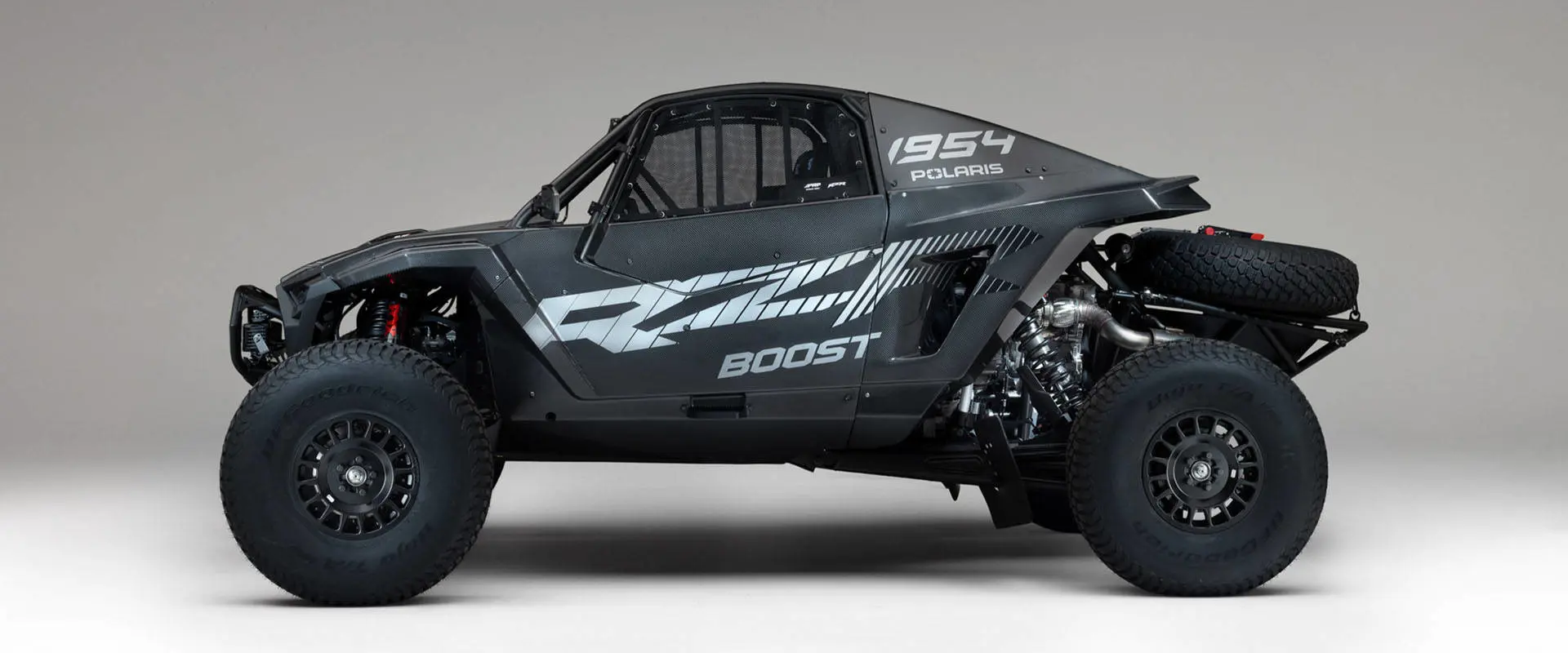 Side view of a 2027 Polaris RZR Pro R Factory Boost SxS featuring carbon fiber bodywork and rear spare tire.