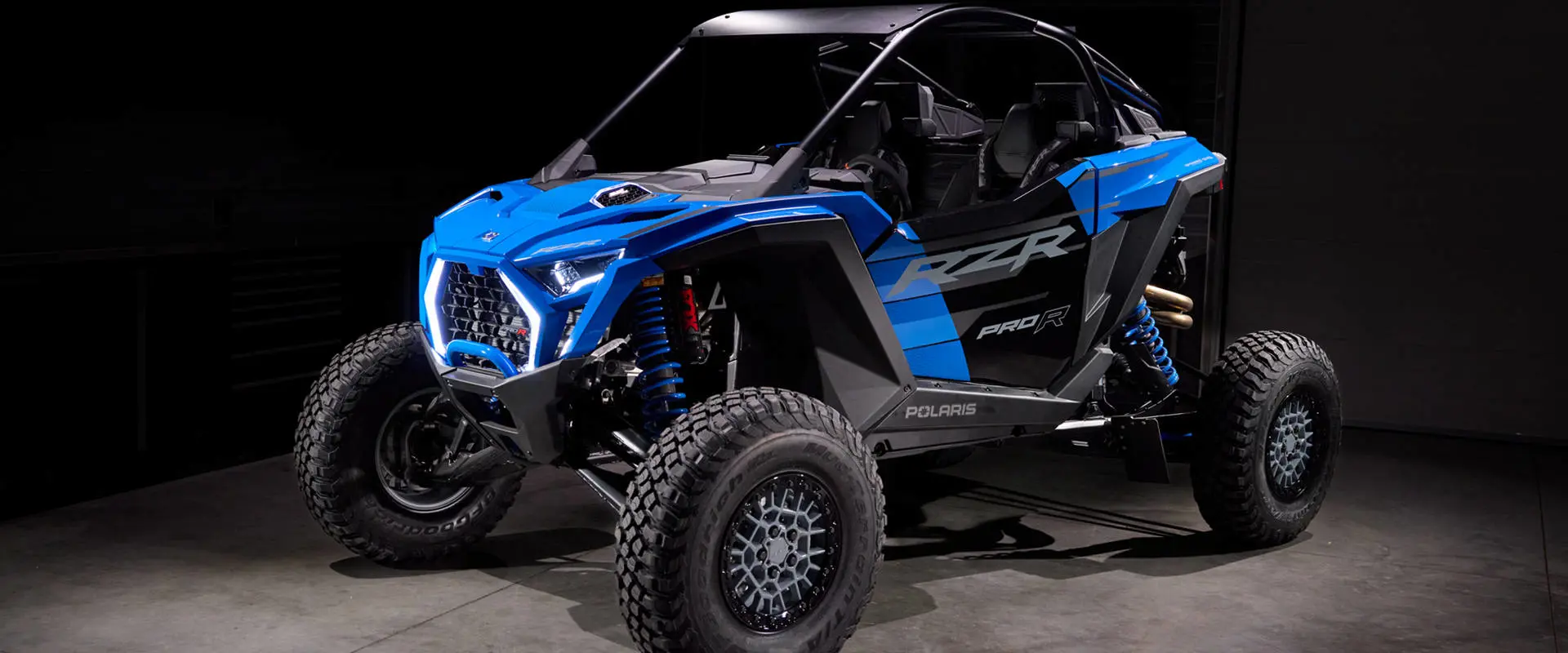Front-angled view of a blue Polaris RZR Pro R Ultra Edition side-by-side in a garage setting with studio lighting.