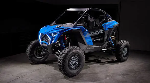 Front-angled view of a blue Polaris RZR Pro R Ultra Edition side-by-side in a garage setting with studio lighting.