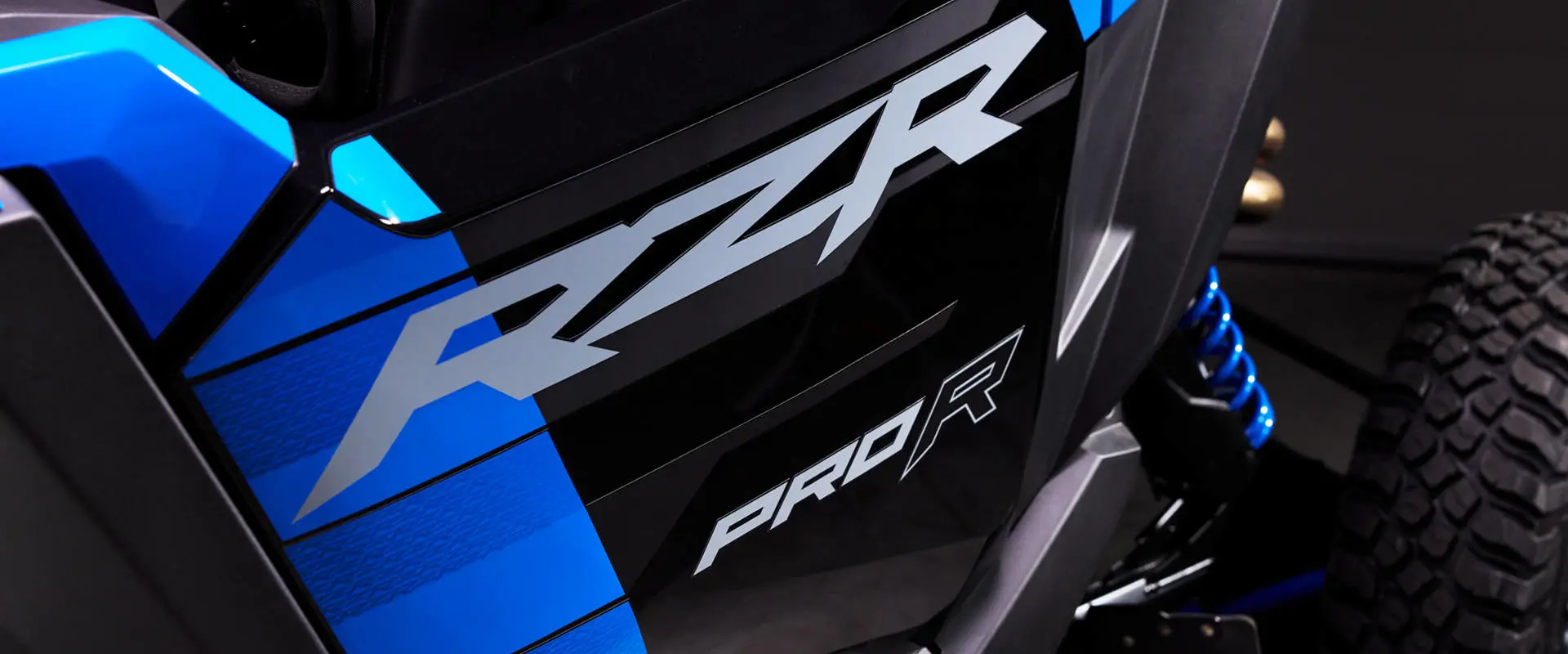 Body panel close-up of the RZR PRO R logo and grey graphics on the Velocity Blue side panel.