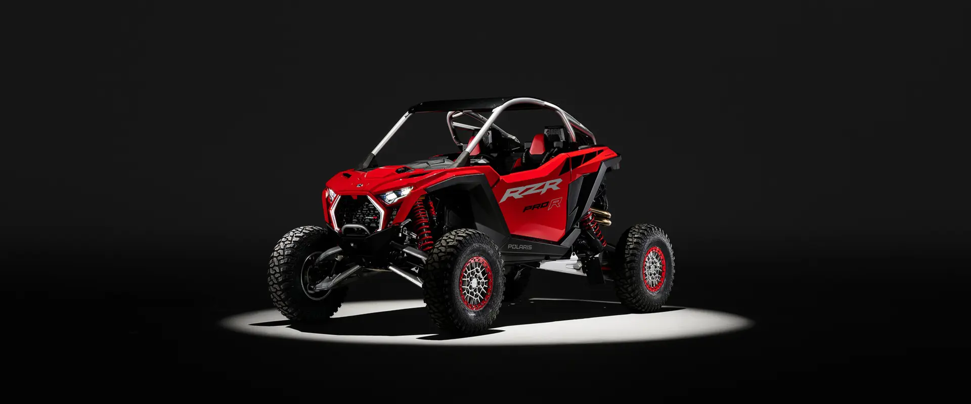 An Indy Red 2026 Polaris RZR Pro R SxS in the spotlight in a dark room.
