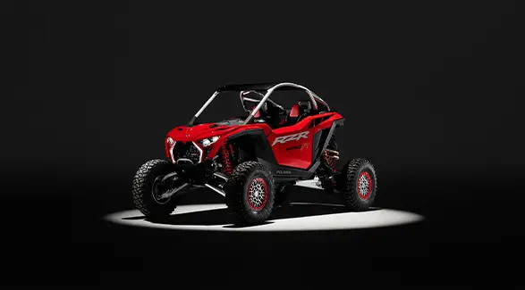An Indy Red 2026 Polaris RZR Pro R SxS in the spotlight in a dark room.