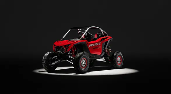 An Indy Red 2026 Polaris RZR Pro R SxS in the spotlight in a dark room.