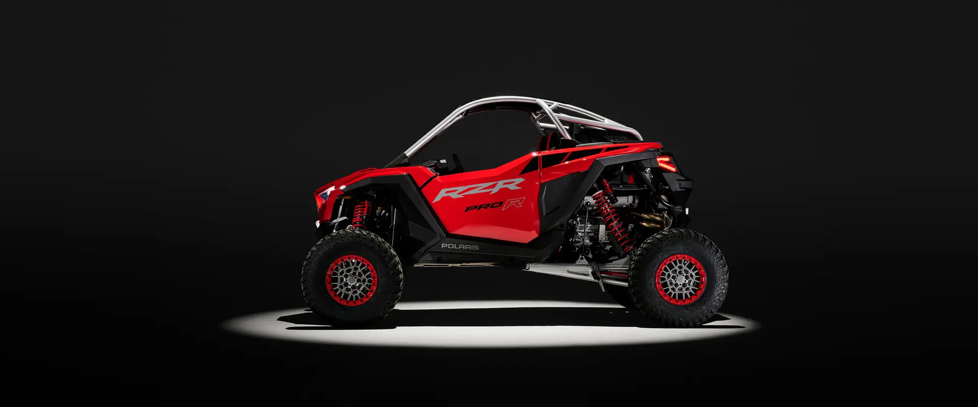 Side profile of a Indy Red 2026 Polaris RZR Pro R SxS in the spotlight in a dark room.