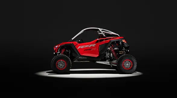 Side profile of a Indy Red 2026 Polaris RZR Pro R SxS in the spotlight in a dark room.