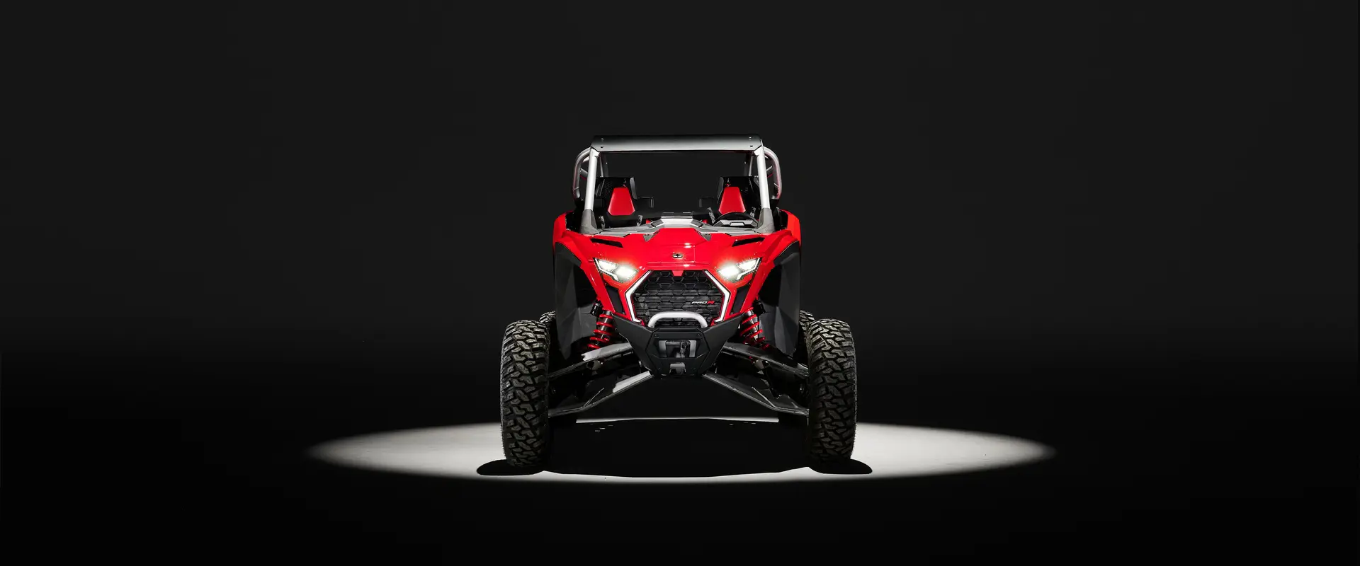 Front end view of a Indy Red 2026 Polaris RZR Pro R SxS in the spotlight in a dark room.