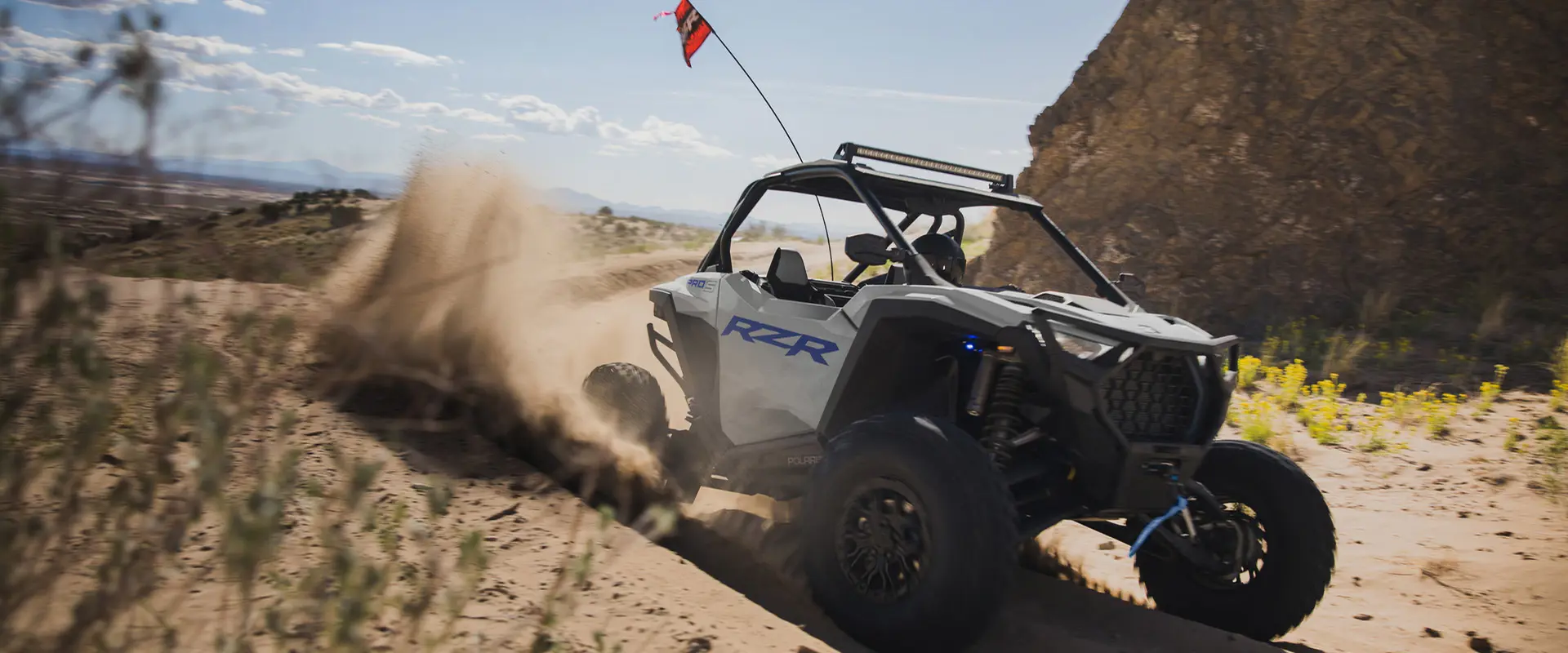 Close-up of the front end of a 2026 Polaris RZR Pro S Sport SxS in Storm Gray taking a tight corner in the dunes.