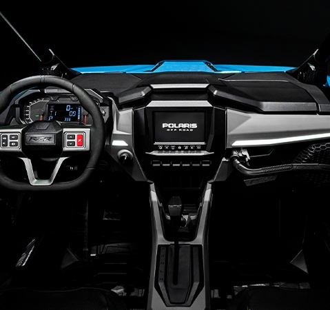 Interior view of a 2026 Polaris RZR Pro XP side-by-side showcasing the optimized driver touchpoints, steering wheel, RIDE COMMAND touch screen and passenger handles. 