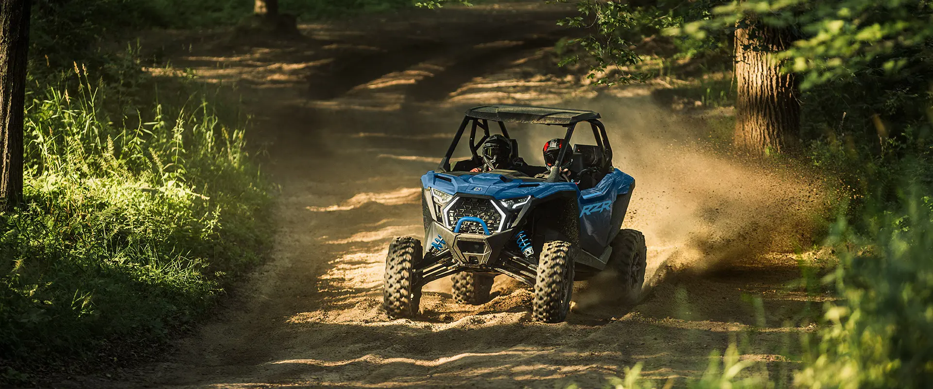 2 conductores en un Side-by-Side Polaris RZR Pro XP de 2026 arrojando arena en un sendero boscoso arenoso y angosto.