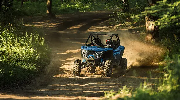 2 conductores en un Side-by-Side Polaris RZR Pro XP de 2026 arrojando arena en un sendero boscoso arenoso y angosto.