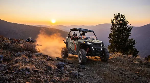 A 2026 Polaris RZR Trail S side by side cruising over rocky terrain at dusk.