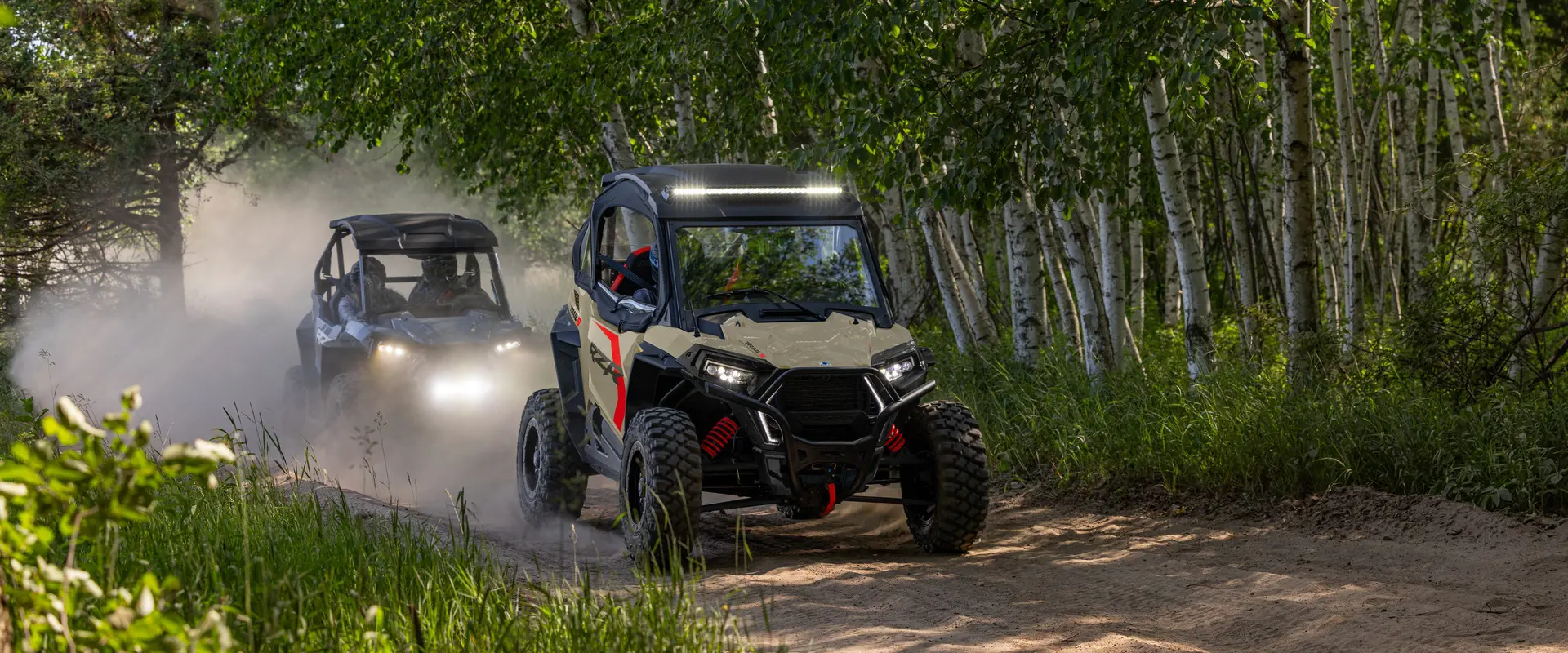 A 2026 Polaris RZR Trail S side by side leading the way on a trail with a 2026 RZR Trail following behind.