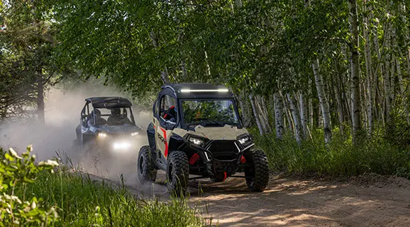 A 2026 Polaris RZR Trail S side by side leading the way on a trail with a 2026 RZR Trail following behind.