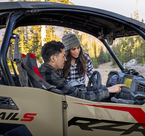 A man pointing to the 7-inch RIDE COMMAND touch screen inside of a 2026 Polaris RZR Trail side-by-side.