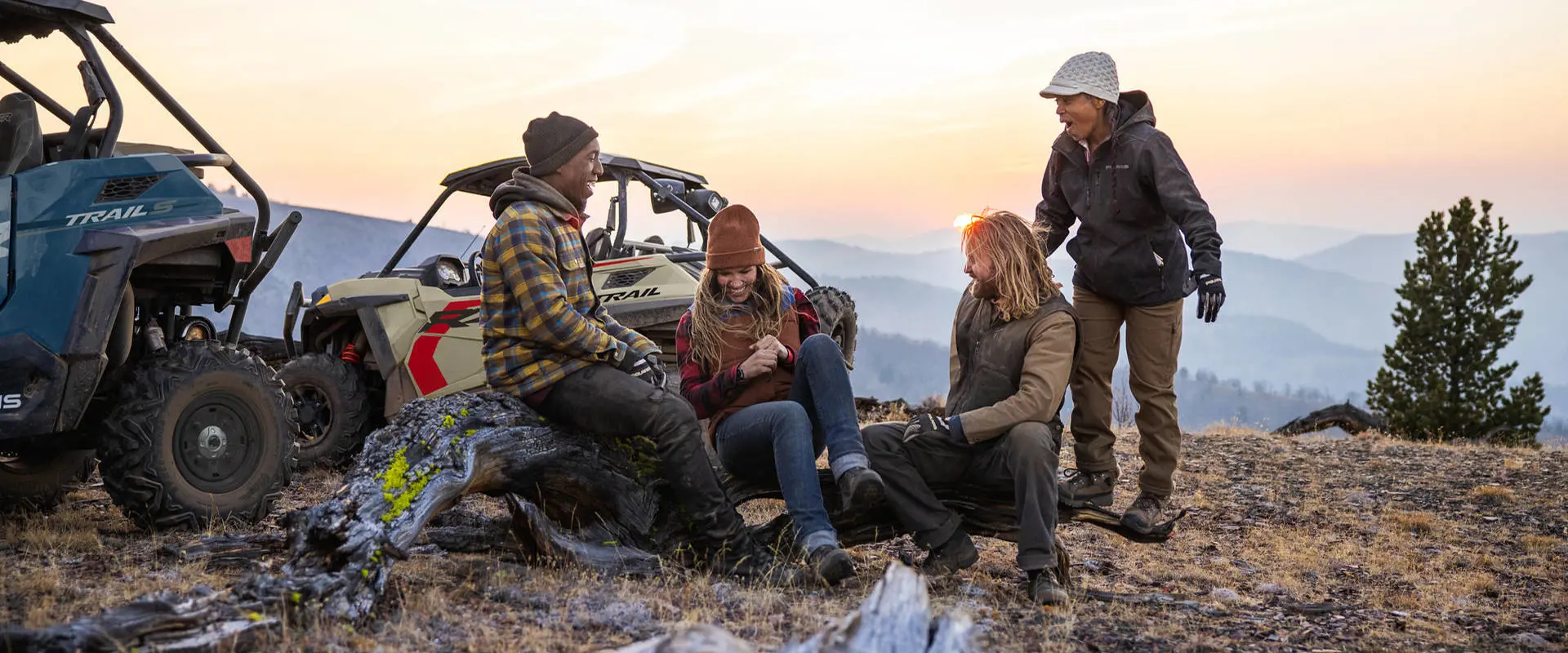 A group of friends relaxing after a ride in their 2026 Polaris RZR Trail side-by-sides.