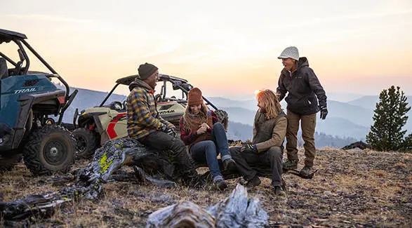 A group of friends relaxing after a ride in their 2026 Polaris RZR Trail side-by-sides.