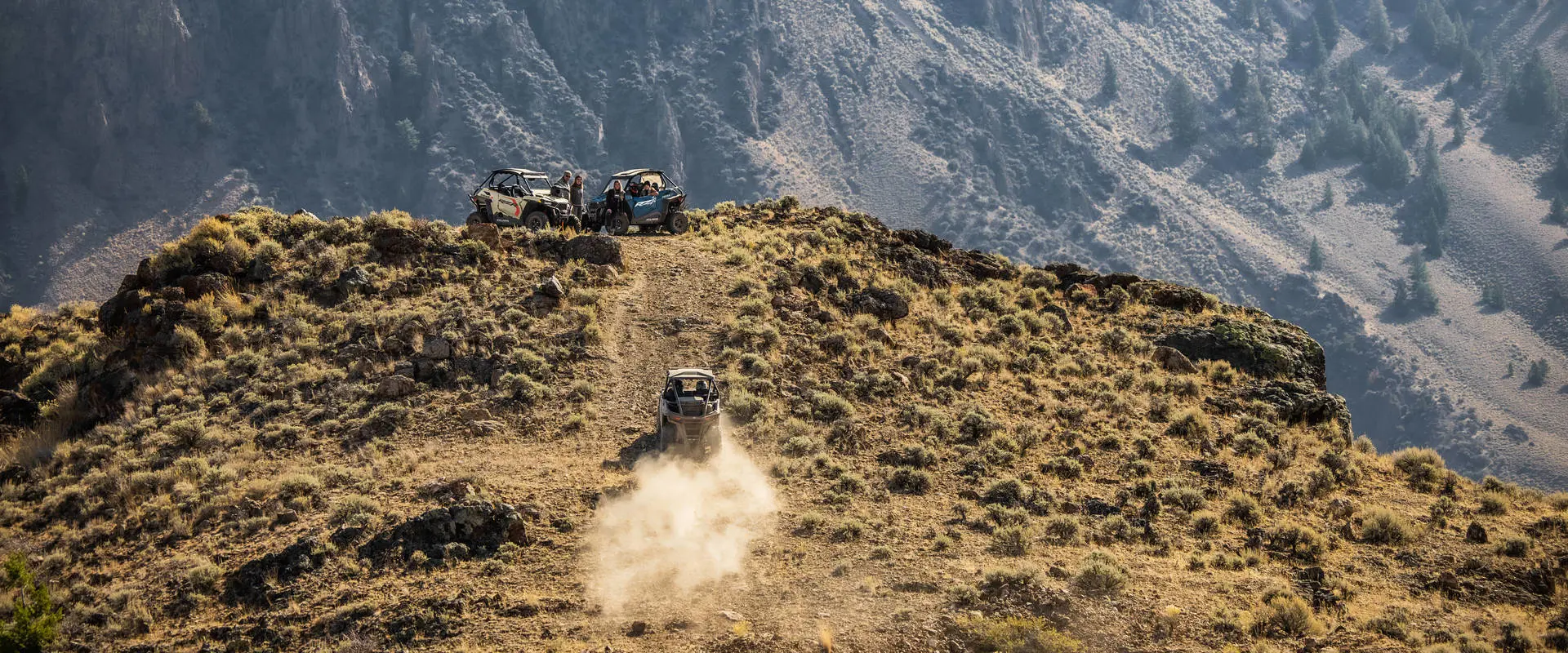 A 2026 Polaris RZR Trail side-by-side climbing a hill to meet two other RZR Trail side by sides.