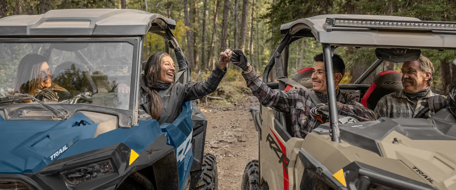 People pounding knuckles while seated comfortably in their 2026 Polaris RZR Trail side-by-sides.