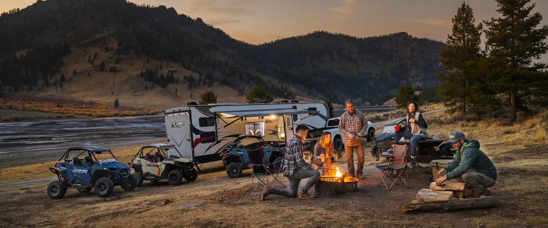 Friends around a campfire relaxing after a day of riding their 2026 Polaris RZR Trail side-by-sides.