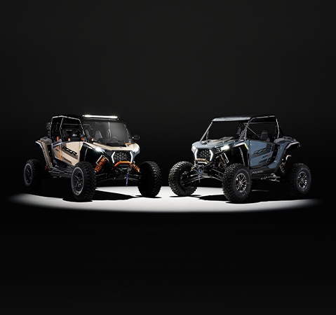 2 accessorized 2026 Polaris RZR XP S side-by-sides with the spotlight on them in a dark room.
