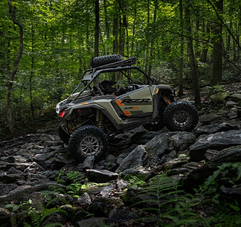 Side profile of a 2026 Polaris RZR XP S side-by-side in a forest traversing rocky terrain and showcasing its 7 percent stronger chassis.