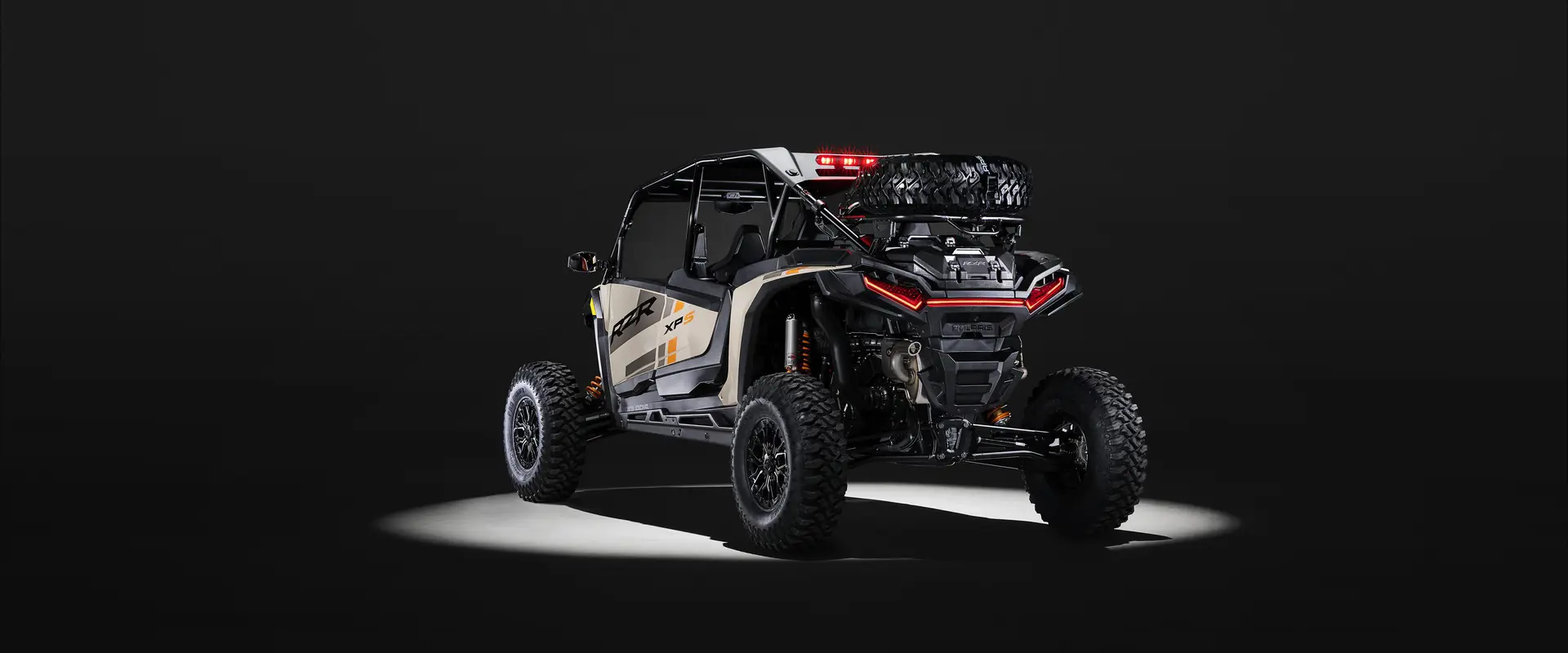 Rear view of a 2026 Polaris RZR XP S 4 SxS entrenched in spotlight in a dark room.