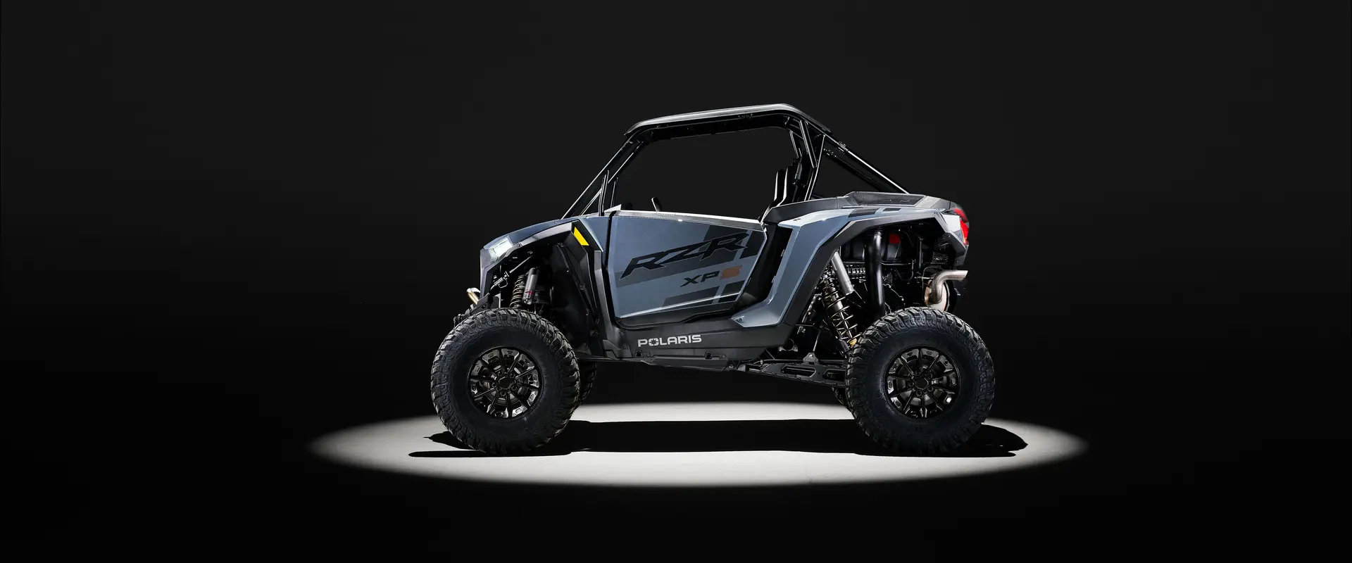 Side profile of a 2026 Polaris RZR XP S SxS entrenched in spotlight in a dark room.
