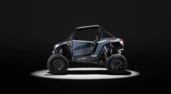 Side profile of a 2026 Polaris RZR XP S SxS entrenched in spotlight in a dark room.