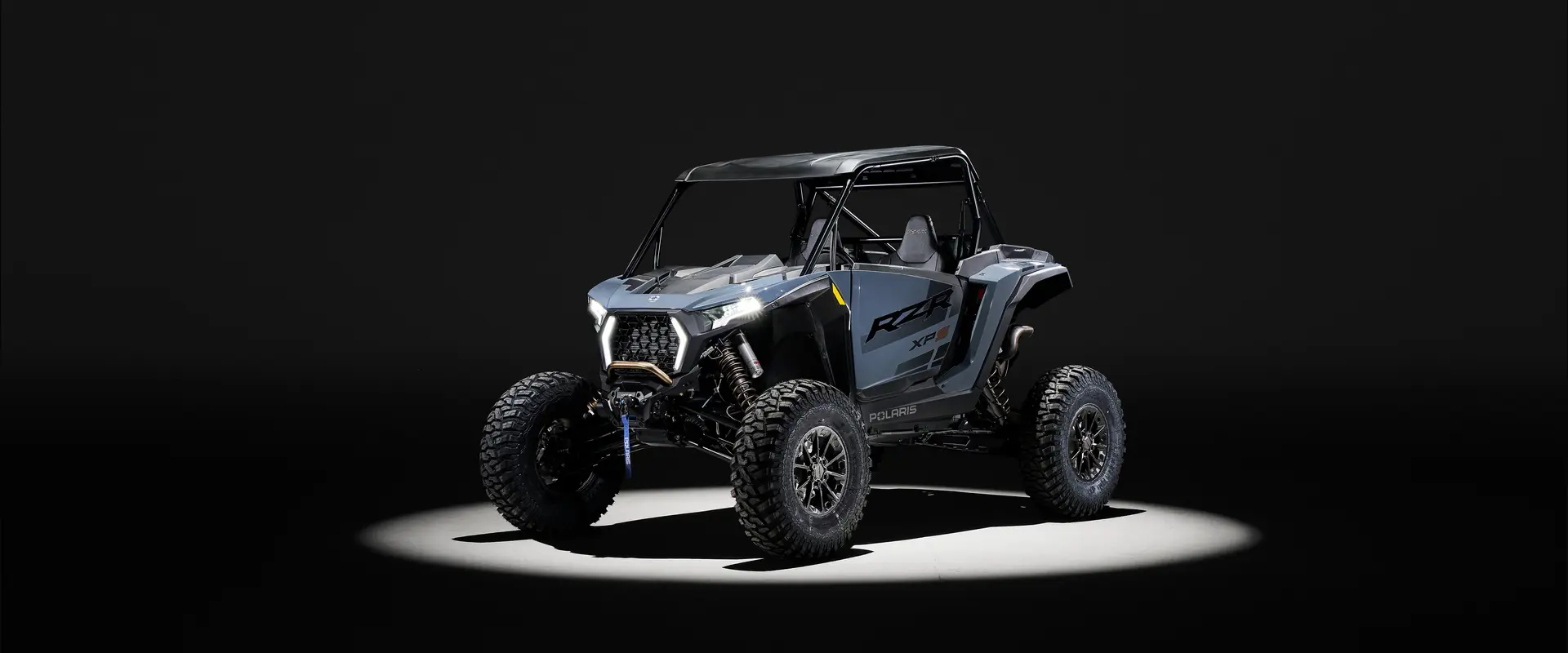 Angled view of a 2026 Polaris RZR XP S SxS entrenched in spotlight in a dark room.