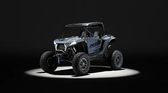 Angled view of a 2026 Polaris RZR XP S SxS entrenched in spotlight in a dark room.