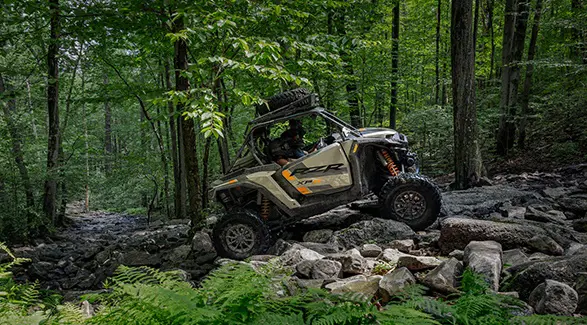 Side profile of a 2026 Polaris RZR XP S side-by-side crawling over rocky terrain in the forest.