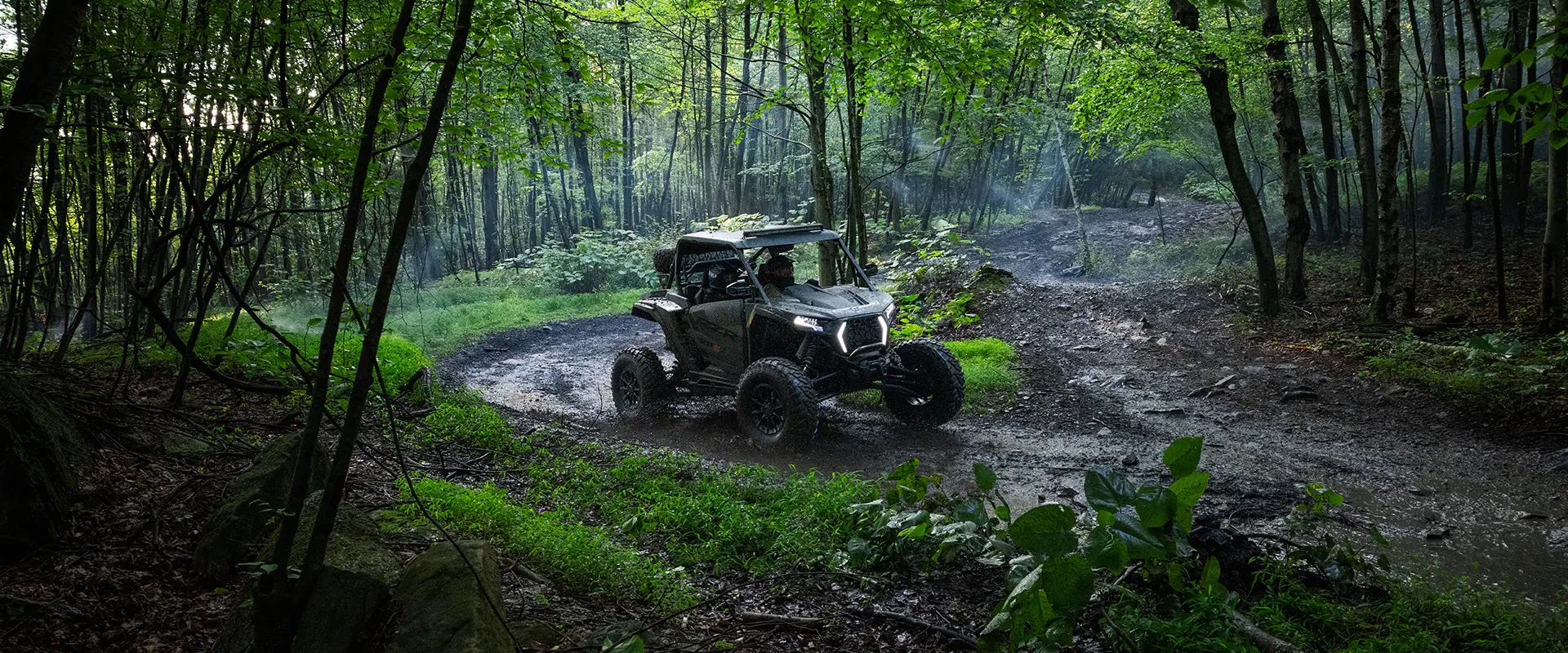 A 2026 Polaris RZR XP S side-by-side driving through the mud in the forest.