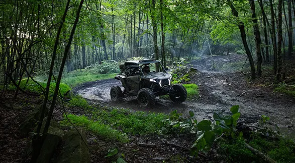 A 2026 Polaris RZR XP S side-by-side driving through the mud in the forest.